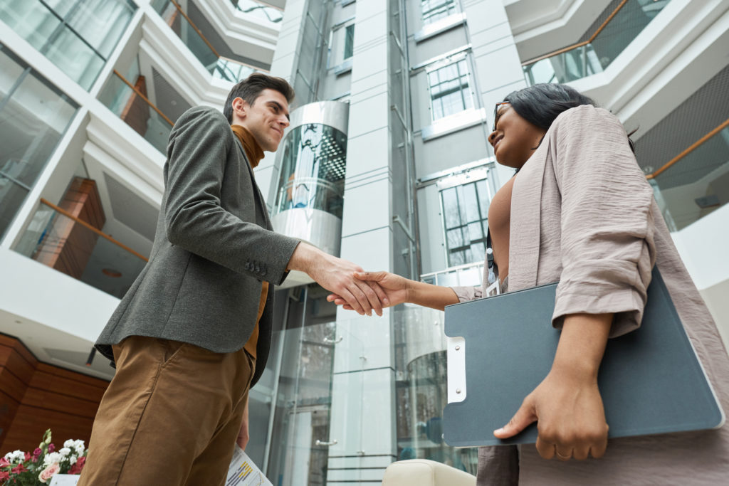 Two business partners standing outdoors with building in the background and shaking hands