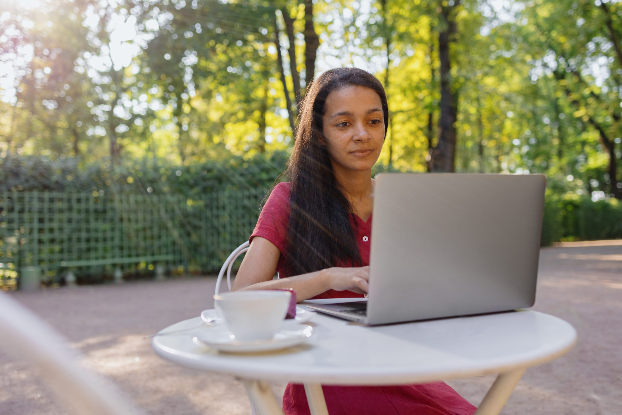 woman in a burgundy dress drinking tea outside on a computer